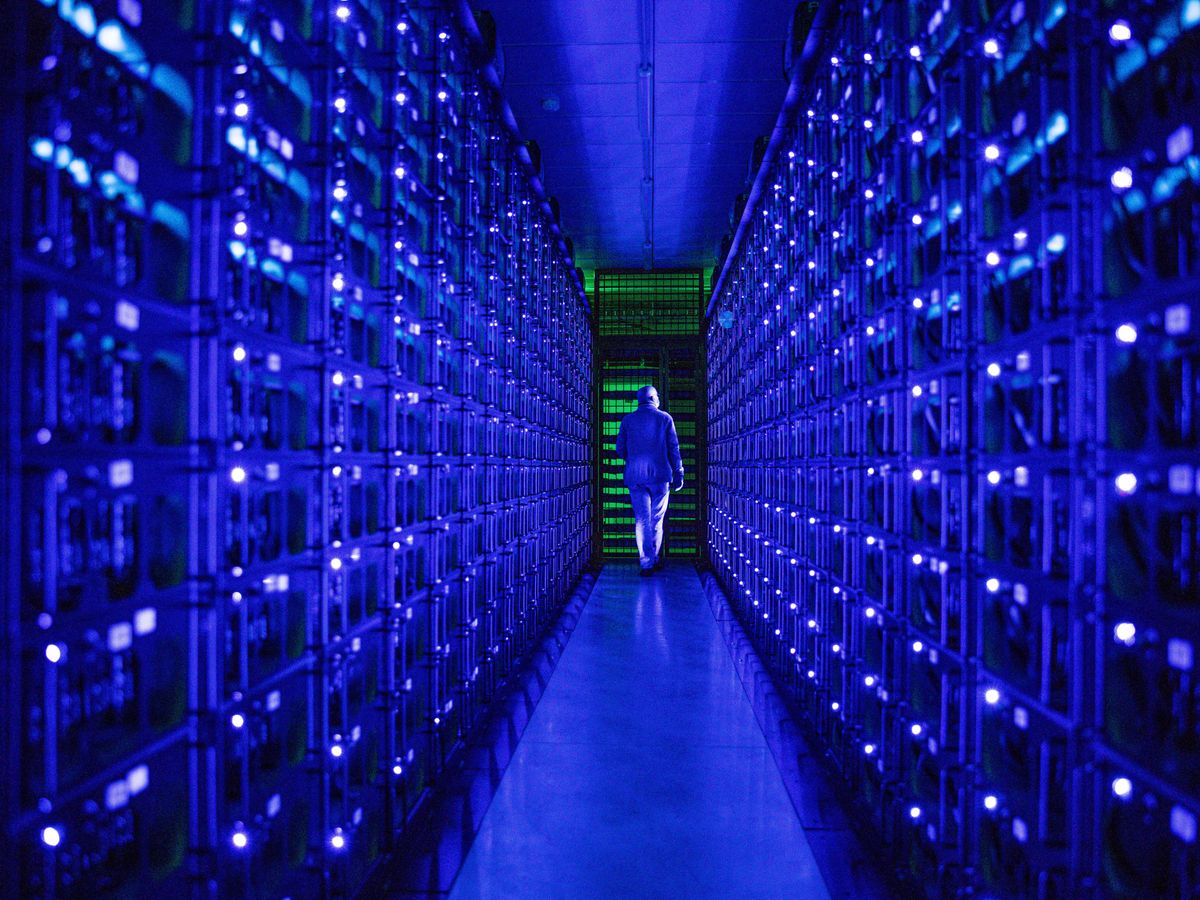 一个巨大的蓝色数据中心。一个穿着白色无尘服的人走向一个绿色照明的房间。