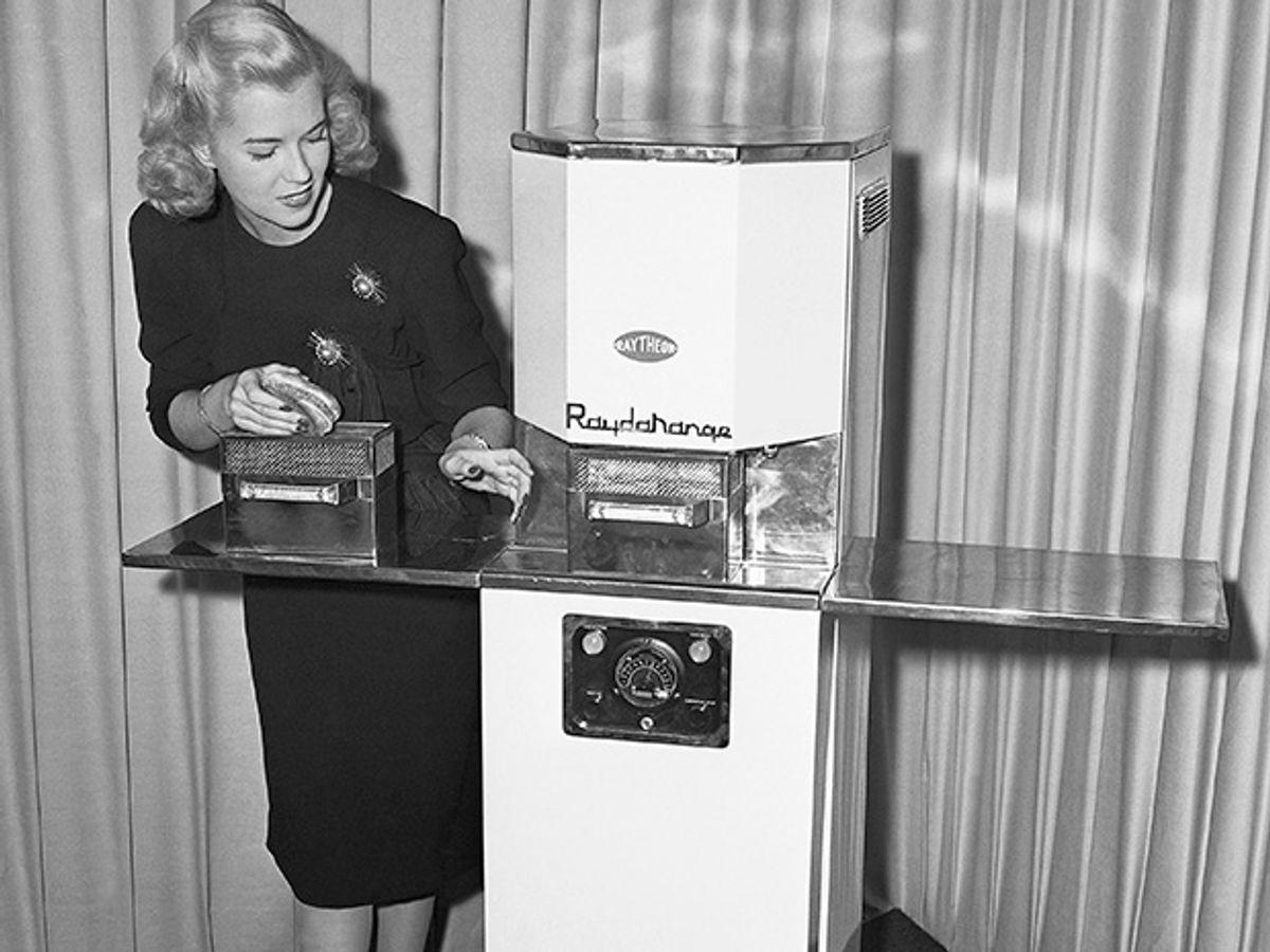 一个女人站在早期微波炉的后面的照片。