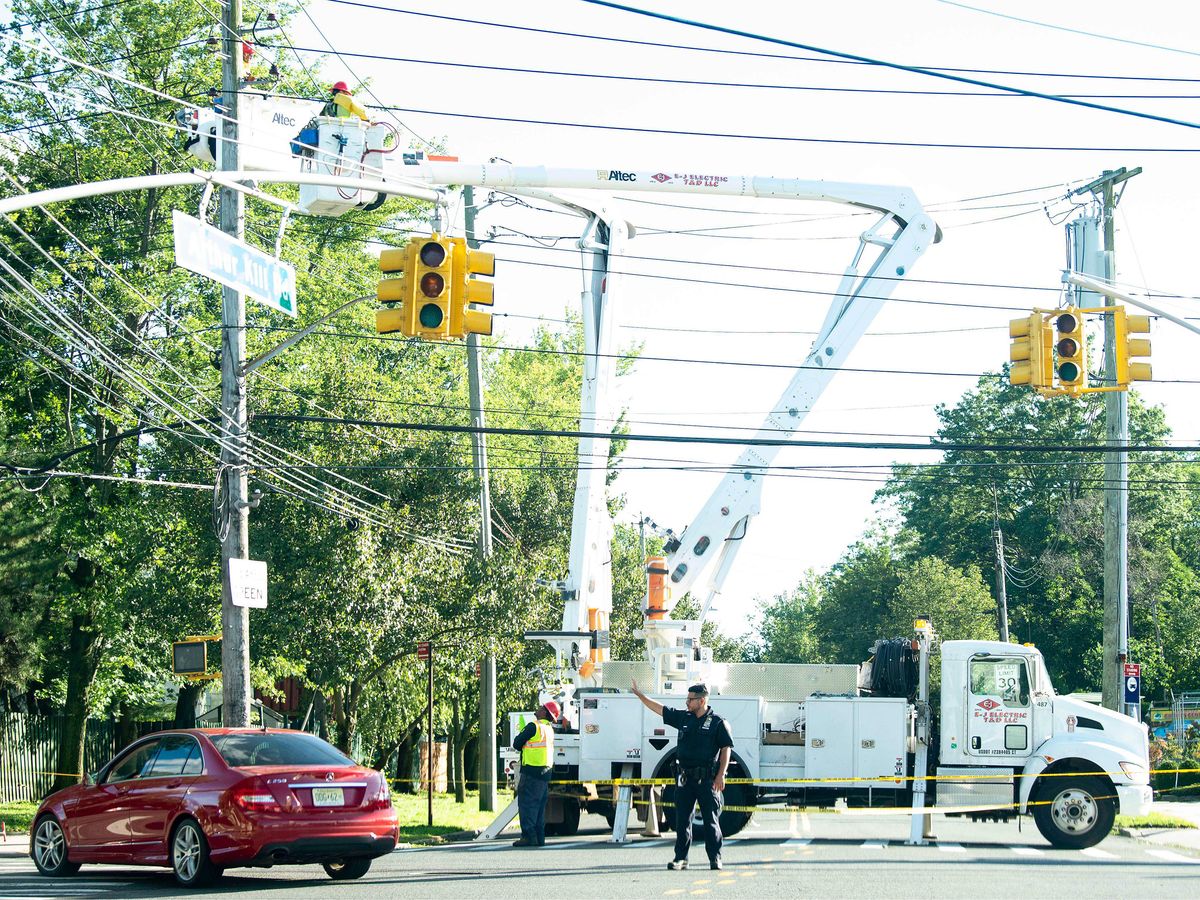 由于热带风暴伊萨亚斯在纽约斯塔顿岛，一名警察指挥交通，爱迪生公司的工作人员正在恢复电力。