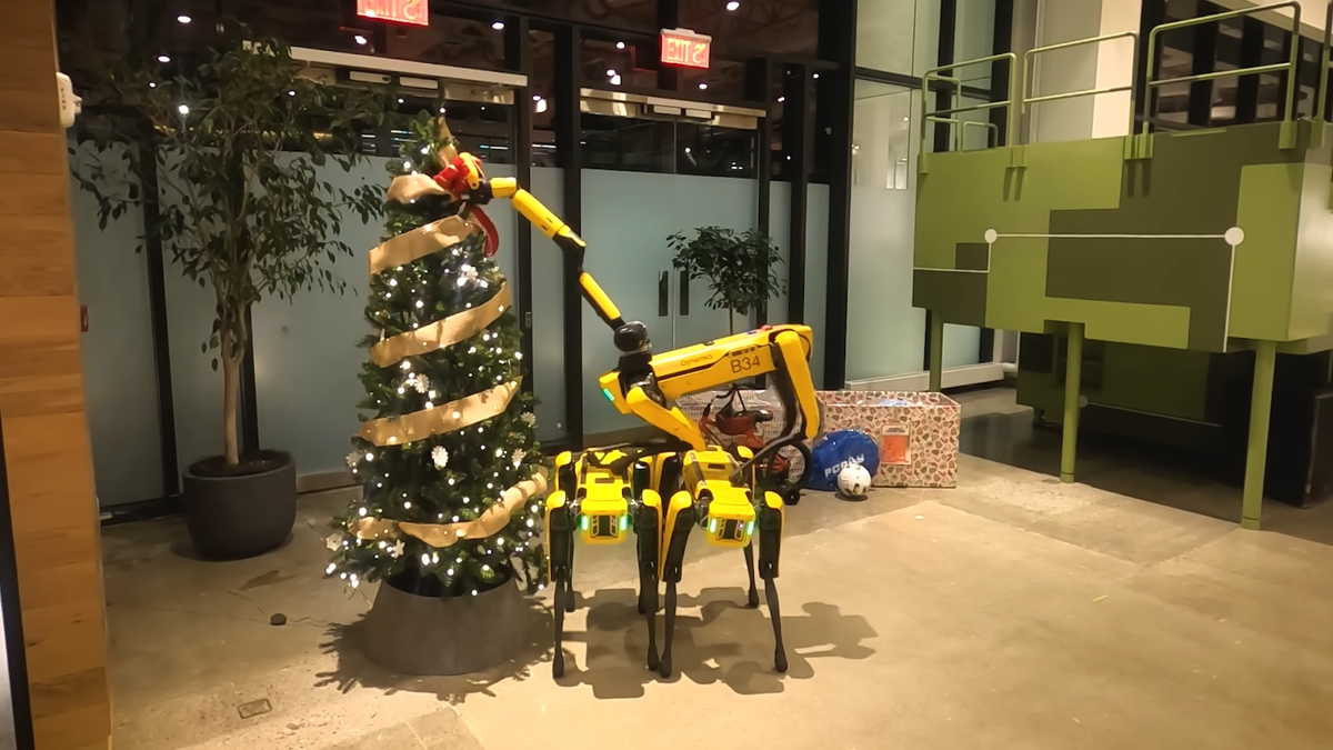 一段视频截图显示，三个黄色四足机器人组成的金字塔在圣诞树顶部放了一个蝴蝶结
