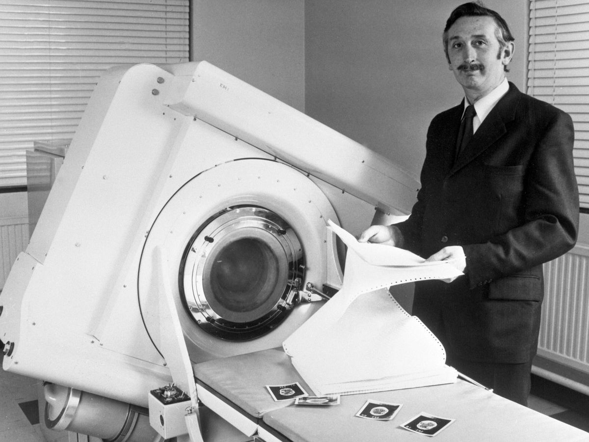 一个西装革履的男人站在一台大型x光机旁的黑白照片