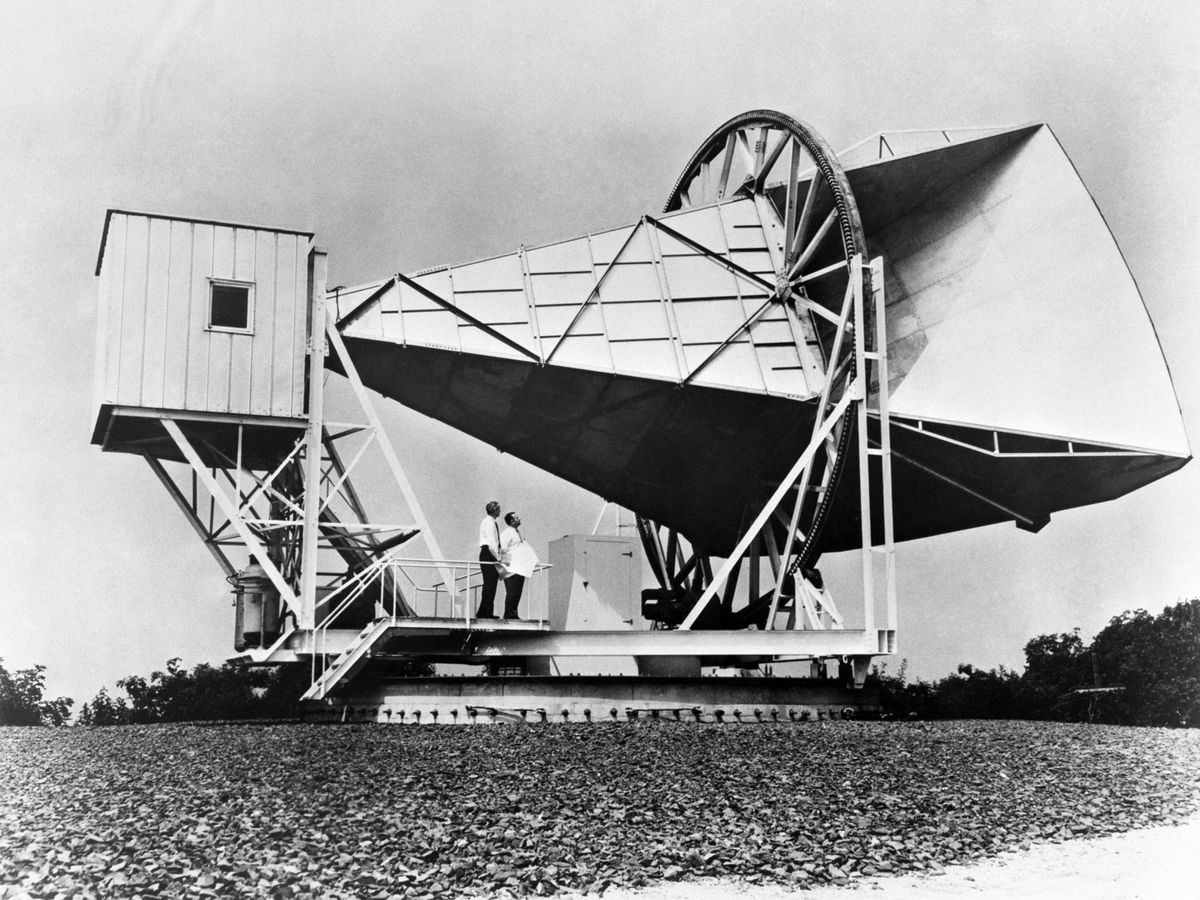 黑白照片，两名男子站在户外一个巨大的锥形结构下