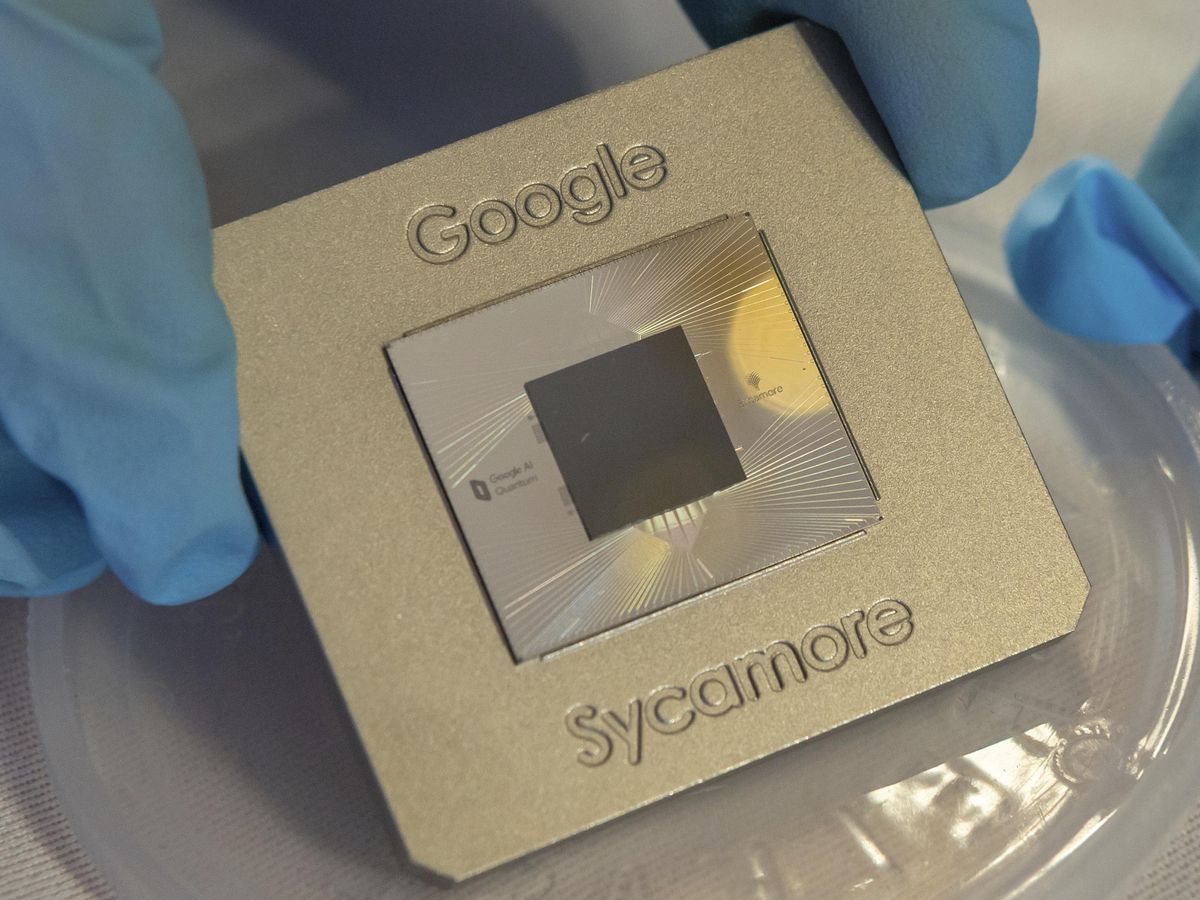 戴着蓝色手套的手指举起一块标有谷歌Sycamore的金属板，上面装有一个方形芯片