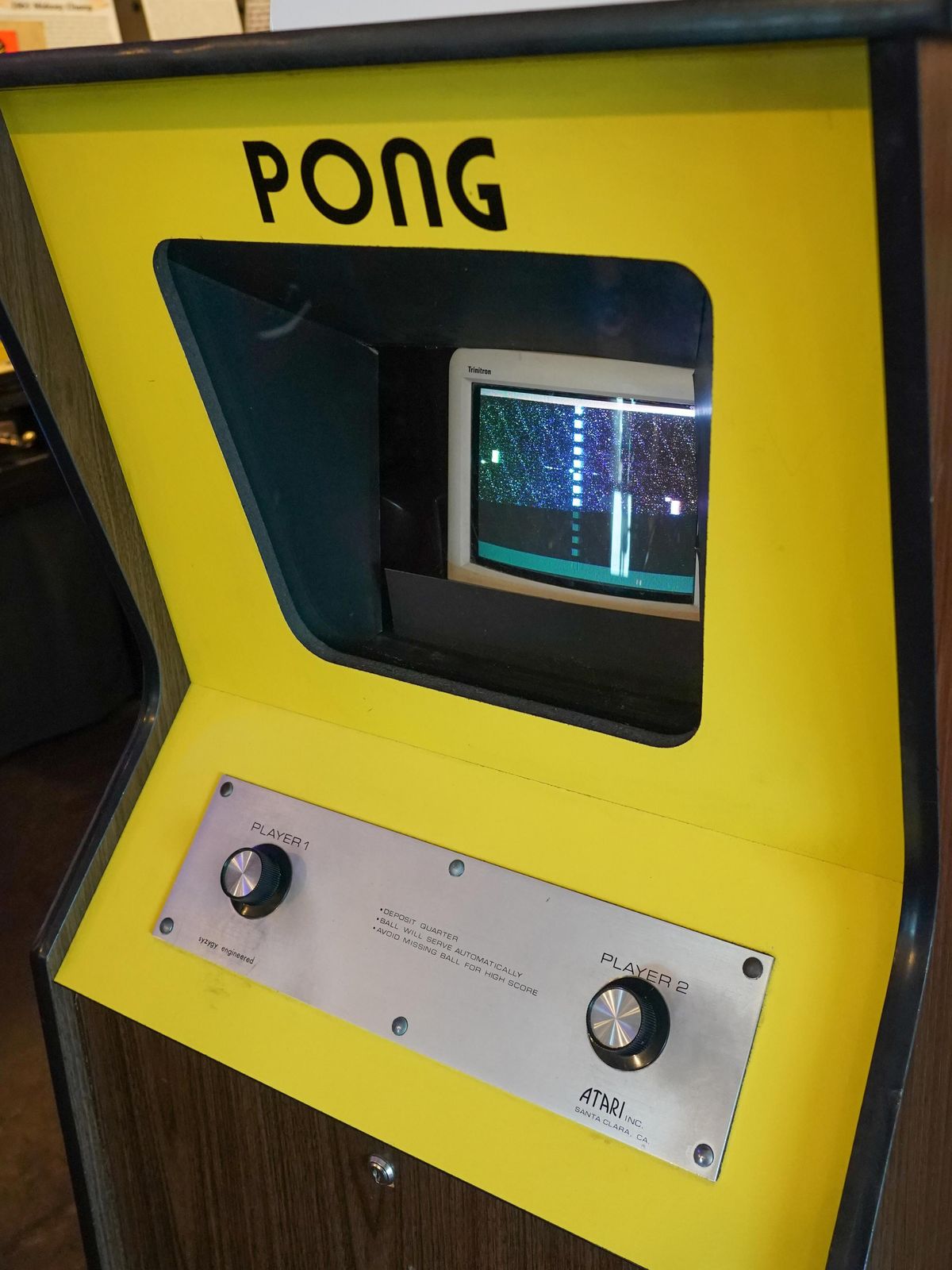 Pong街机游戏在黄色的柜子里装有黑白电视显示屏，两个旋钮上分别标注着玩家1和玩家2，可见雅达利的标志。