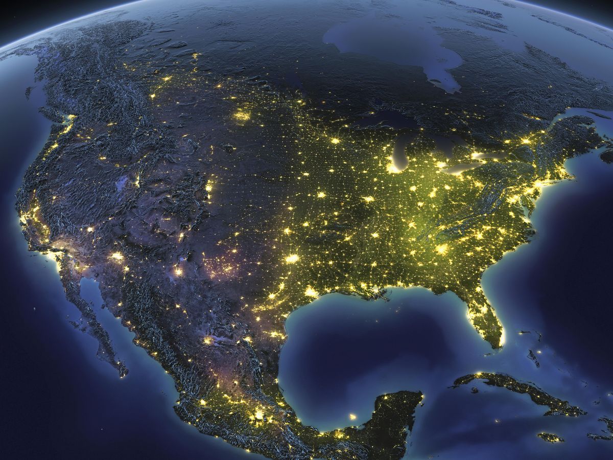 美国夜间的卫星俯视图。陆地是灰色的，全国各地都有亮黄色的灯光。